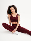 a woman sitting on the floor in a maroon sports bra top and leggings