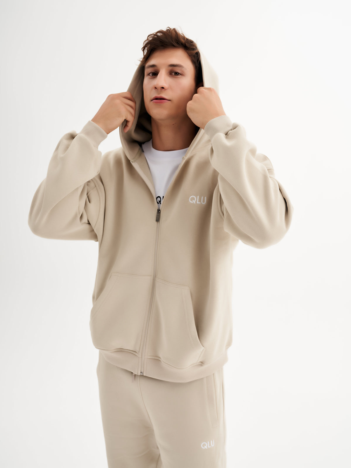 a man in a beige hoodie is holding his hands to his ears