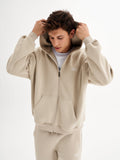 a young man in a beige tracksuit is covering his ears