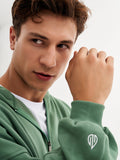 a man in a green sweatshirt holding his hand up to his face