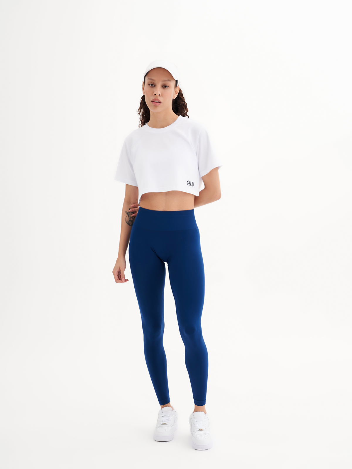 a woman wearing a white crop top and blue leggings