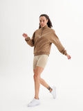 a woman in a brown sweatshirt and beige shorts