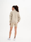 a woman wearing a beige sweatshirt and shorts