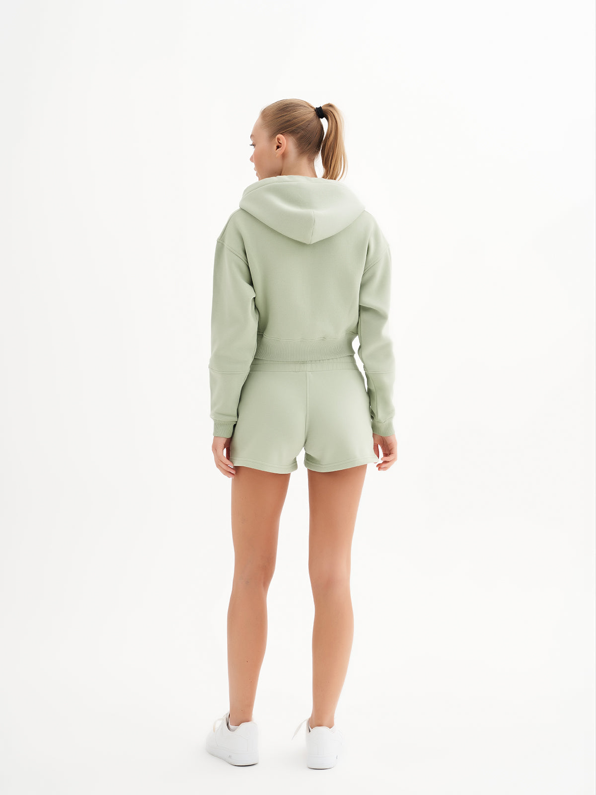 a woman wearing a green sweatshirt and shorts