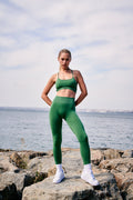 a woman in a green sports bra top and leggings stands on a rock